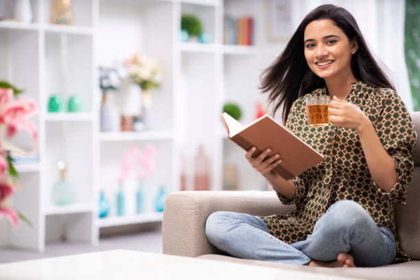 mujer en casa sofá sentado - foto de stock - infusión té bebida fotografías e imágenes de stock