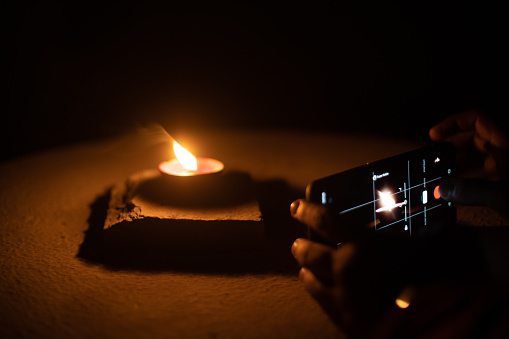 Man woman taking low light pictures of a diya oil lamp with a mobile phone for sharing images on the hindu festival of diwali. Shows the immense influence of social media and technology like low light capable cameras on traditional festivals like the hindu festival