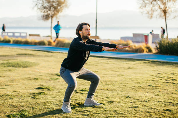 istock Young caucasian man performing squats before jogging on footpath in park. 1284970505