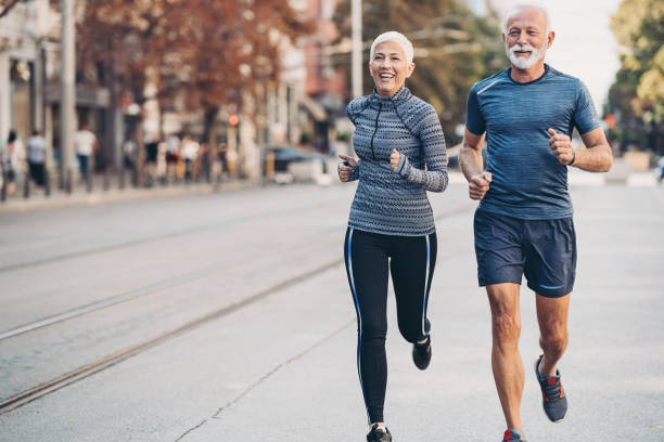 anziano uomo e donna anziano jogging fianco a fianco sulla strada - workout foto e immagini stock