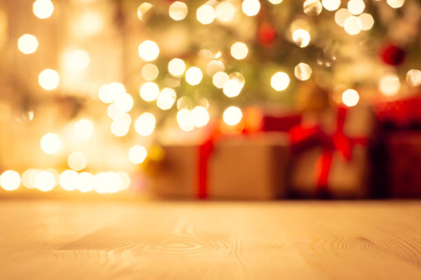 Blurred view of christmas tree in bright warm lights and beautiful presents under it, focus on the floor.