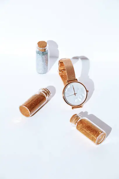 Watch, sequins bottles in whitespace. New Year, holiday, Christmas concept. Minimalism, Still life art