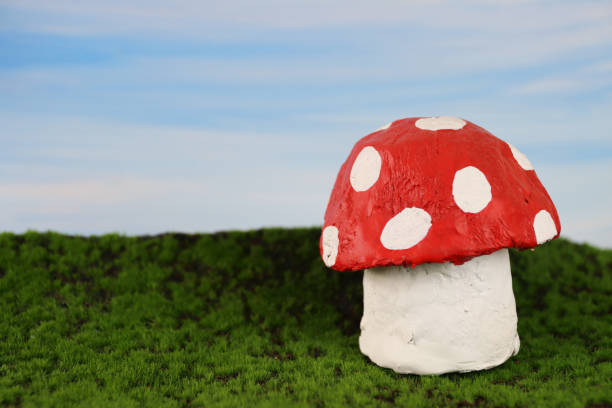 Stock photo showing a close-up view of handmade red and white spotted toadstool modelled from papier mache, in an agricultural farm field scene with green grass and blue sky.