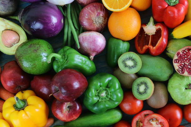 Stock photo showing a background of fruits and vegetables in various states of being cut up. Whole and halved avocado, lettuce, red onion, oranges, red, green and yellow bell peppers, red cabbage, courgettes, carrots, red apples, kiwi, tomatoes, potato, bananas, pomegranate. marco completo, imagen de primer plano de grupo entero y frutas y verduras cortadas a la mitad, aguacate, lechuga, cebolla roja, naranjas, pimiento rojo, verde y amarillo, repollo rojo, calabacines, zanahorias, manzanas rojas, kiwi, tomates, patata, pláta