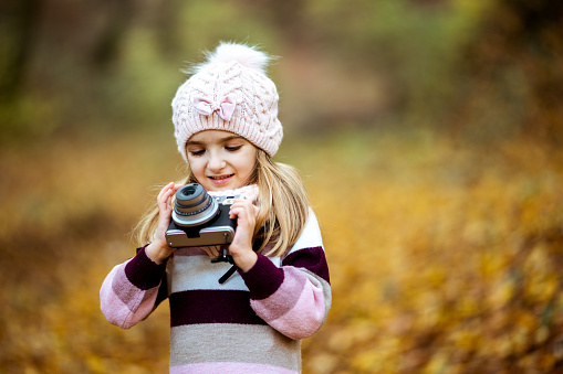Happy girl plays with the photo camera in the beautiful autumn forest.