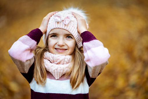 Little cheerful girl wearing knitted, scarf and a colourful sweater seen in the autumn forest.