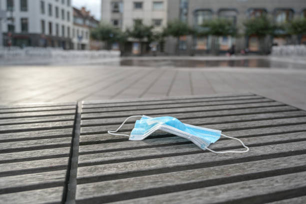 used surgical face mask against infection with coronavirus and covid-19 carelessly left lying on a bench in the city center, copy space - one way road sign sign blank imagens e fotografias de stock