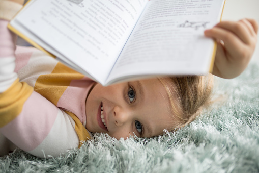 Close-up of an Adorable little girl lying on bedroom floor and reading a book