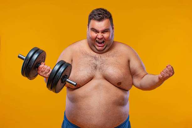 istock Fat man doing workout traning with dumbbells. Happy guy isolated over yellow background. 1284983952