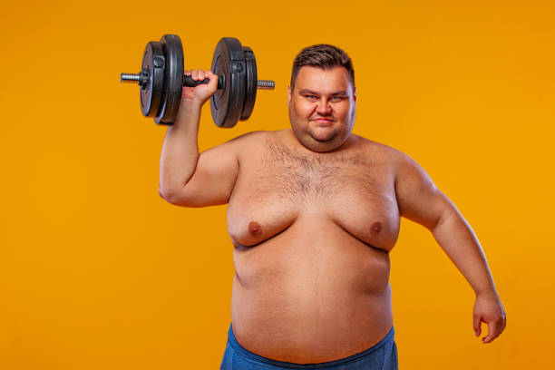 istock Fat man doing workout traning with dumbbells. Happy guy isolated over yellow background. 1284983965