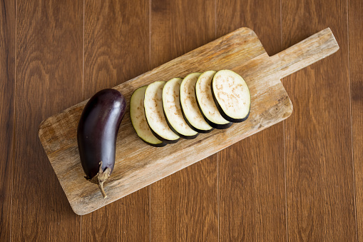 Close up of whole and sliced eggplants on cutting board on wooden table