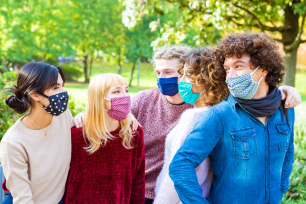 istock Young people having fun around city park during coronavirus outbreak.Happy multiethnical friends wearing face protective masks and laughing together.new normal lifestyle.group of students chilling outdoors 1284988704