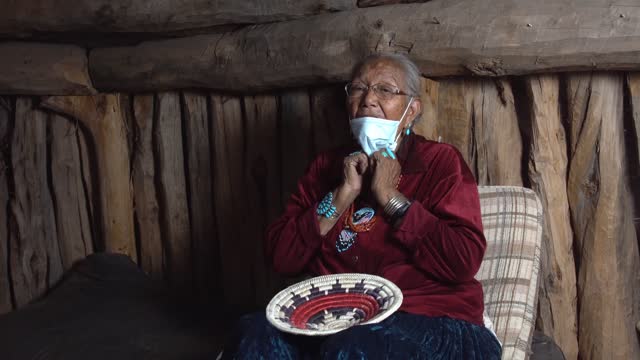 Navajo Grandma sitting in her Hogan in Monument Valley Arizona wearing a face mask to prevent contracting the Corona or Covid-19