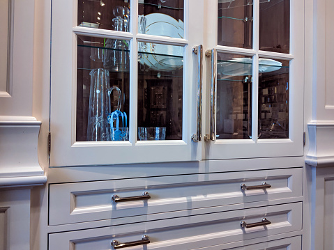 View of a white, glass built-in display cabinet in a kitchen, displaying fine china dishes and crystal pitchers