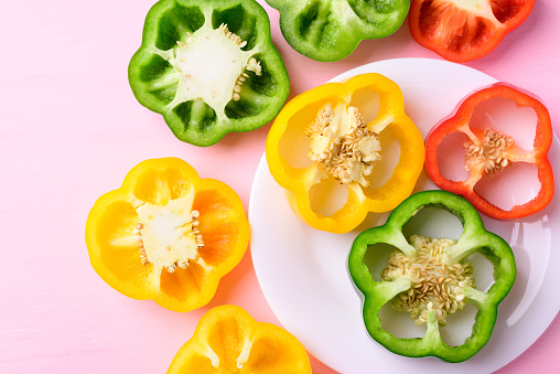 Sliced green, yellow and red bell peppers on white plate with pink background, Top view
