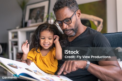 istock Affectionate father reading book with adorable mixed race daughter 1284998990