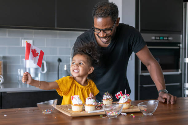 Father and daughter decorate cupcakes while celebrating Canada Day at home A cute mixed race girl her father decorate cupcakes together while celebrating Canada Day at home. canada day photos stock pictures, royalty-free photos & images