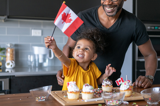 A cute mixed race girl her father decorate cupcakes together while celebrating Canada Day at home.