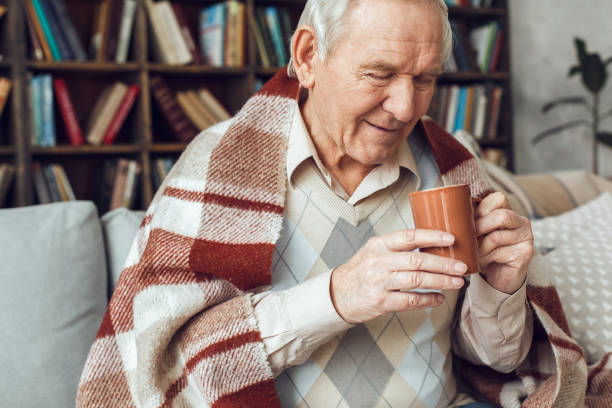 istock Senior man alone sitting at library sick covered with plaid looking at cup of coffee 1284999023