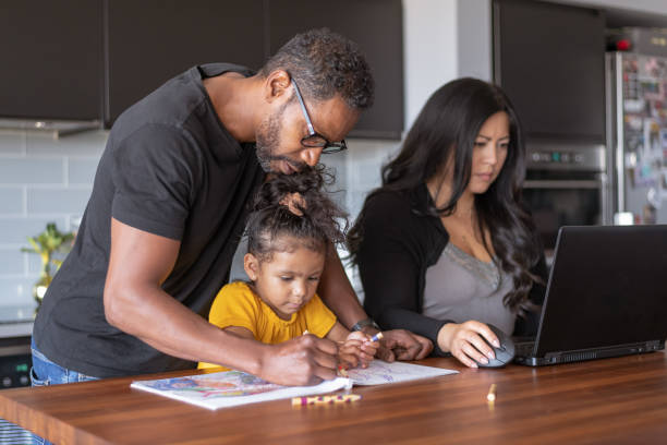 istock Father helping daughter with school assignment while wife works on laptop computer 1284999035