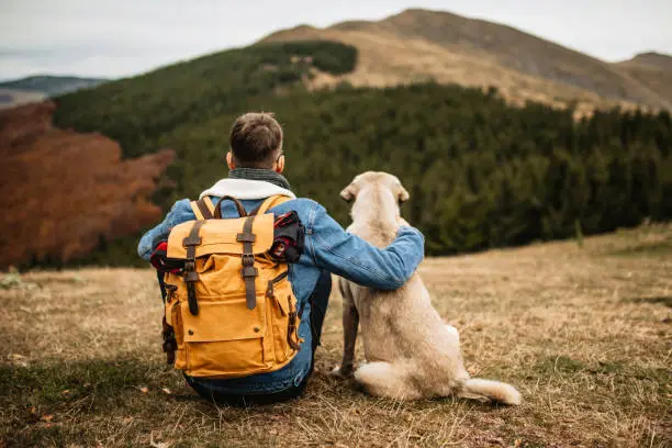 Photo of Hiker with backpack and his dog resting on mountain