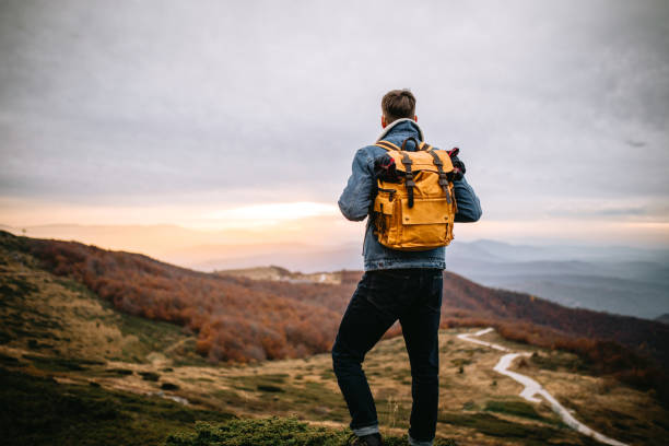 Young handsome hiker standing on the mountain peak at the end of day, observing nature, enjoying the sunset.