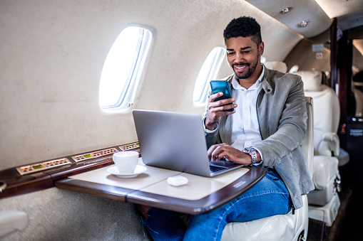 Young casually dressed businessman smiles while looking at his smart phone during the first class flight in the private airplane.