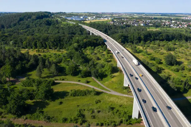 Car traffic on a highway bridge over green forest, viewed from above.