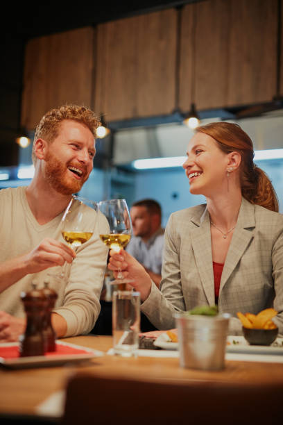 junge lächelnde, glückliche paar verliebt sitzen im restaurant zum abendessen und toasten mit weißwein. - restaurant dining couple dinner stock-fotos und bilder