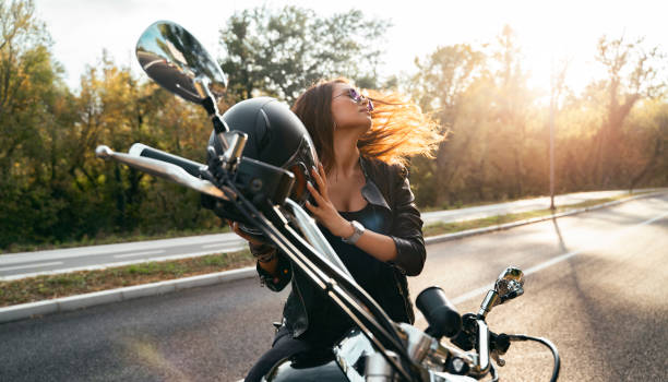 atractiva joven mujer sentada en bicicleta, tomando el casco y echando su pelo - motorcycle women helmet sensuality fotografías e imágenes de stock
