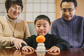 丸い餅にマンダリンオレンジを置くアジアの祖父母と孫