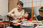 日本の部屋の食卓で、お飾ちりり、日本の新年料理を食べる日本人の祖母と孫
