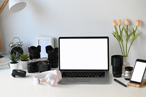 Front view of graphic designer or photographer workspace with empty screen laptop and camera accessory.