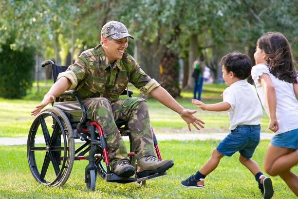 Cheerful kids meeting military dad and running to disabled man Cheerful kids meeting military dad and running to disabled man in camouflage with open arms for hug. Veteran of war or returning home concept wheelchair photos stock pictures, royalty-free photos & images