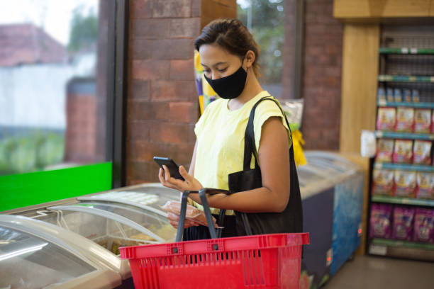 mulher do sudeste asiático verificando sua lista de compras no telefone inteligente antes de comprar comida congelada - southeast asian ethnicity fotos - fotografias e filmes do acervo