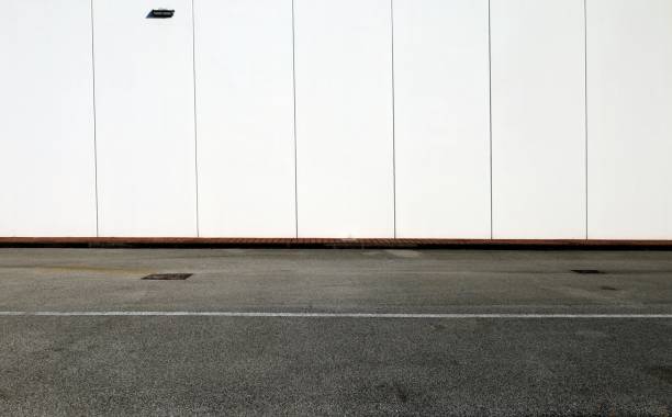 istock White concrete wall with vertical blocks, a brown sidewalk and an asphalt road. 1285045114