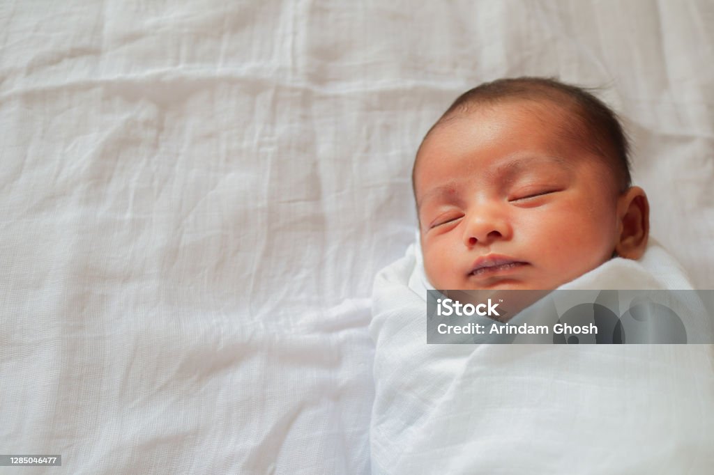 a one month old baby sleeping and swaddled in white cloth lying in white cloth background. Newborn Stock Photo