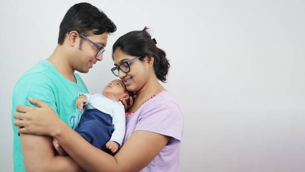 a young man with his wife and newborn kid looking at the baby isolated in white background. - facial expression child asia asian and indian ethnicities imagens e fotografias de stock