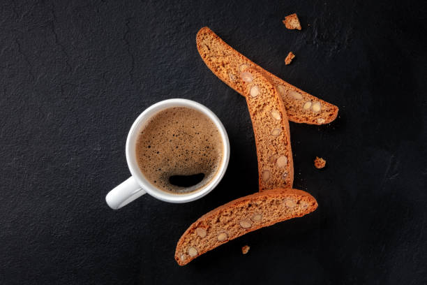 biscotti. biscotti di mandorle italiani con una tazza di caffè, scattati dall'alto su uno sfondo nero - biscotti italian cuisine italian culture breakfast foto e immagini stock