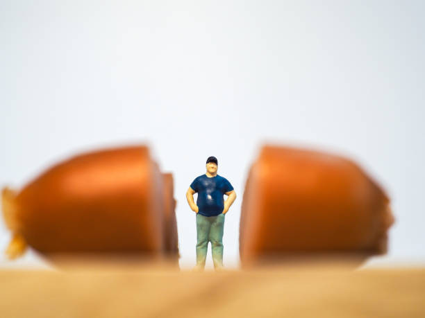 istock Miniature people : Close up fat man standing with sausages isolated on white background 1285050308