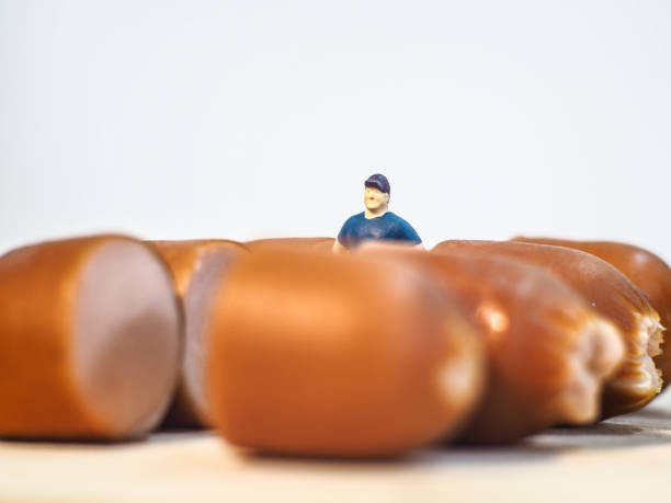 istock Miniature people : Close up fat man standing with sausages isolated on white background 1285050314