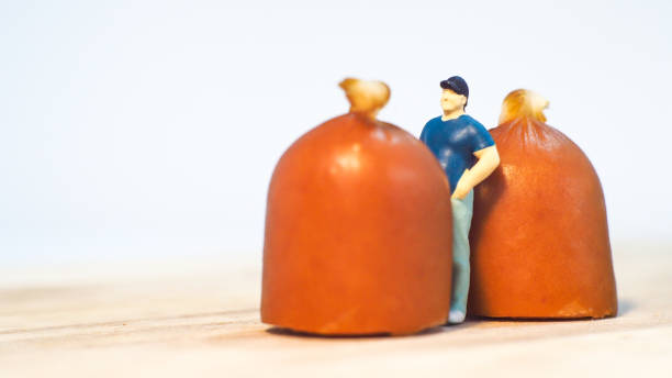 istock Miniature people : Close up fat man standing with sausages isolated on white background 1285050368