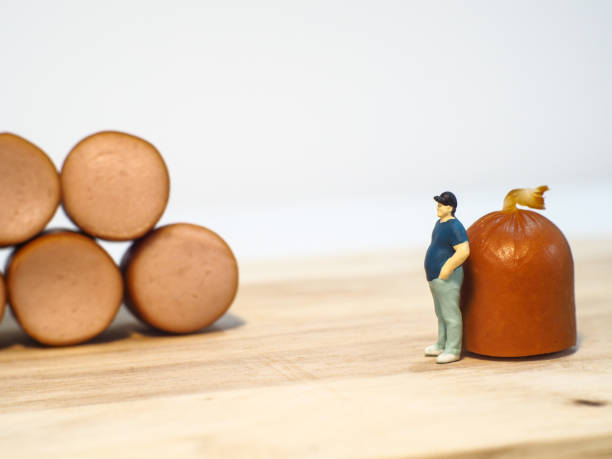 istock Miniature people : Close up fat man standing with sausages isolated on white background 1285050376