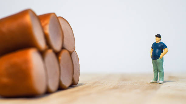 Miniature people : Close up fat man standing with sausages isolated on white background