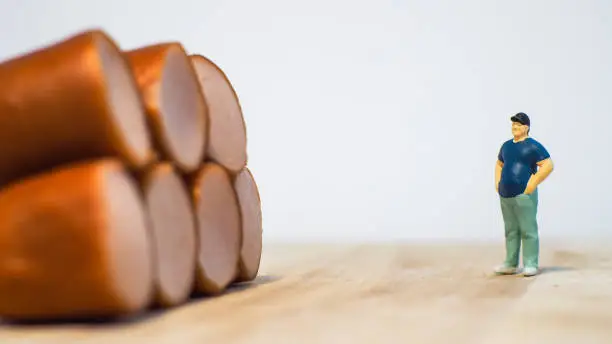 Photo of Miniature people : Close up fat man standing with sausages isolated on white background