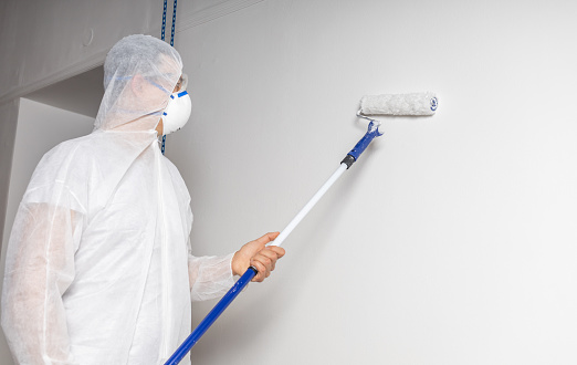 man with paint roller and face mask dressed in white protective suit . High quality photo