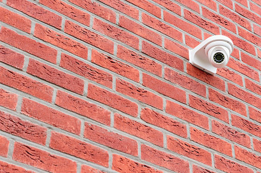 Low angle view on white cctv security camera mounted on a red brick wall. Security concept, big brother is watching