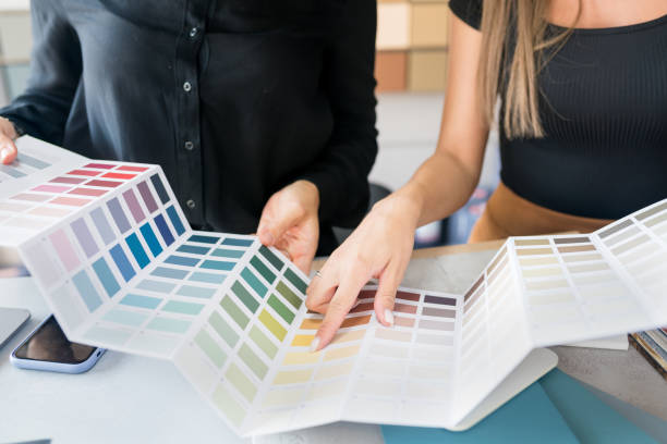 close-up of two women choosing samples of wall paint. interior designer consulting a client looking at a color swatch. house renovation concept - color swatch print color image spectrum imagens e fotografias de stock