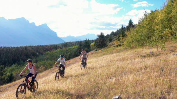 istock Mountain bikers ride along an open field above a valley and mountains 1285060053