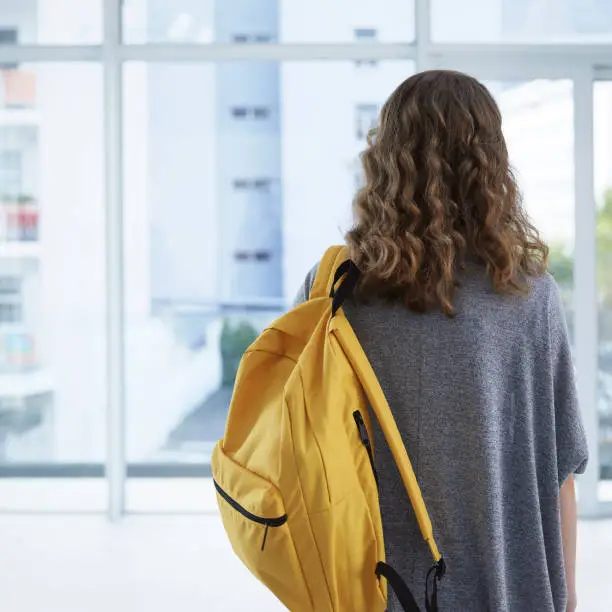 Lonely student enters the school classroom. She pauses while looking for a friend.